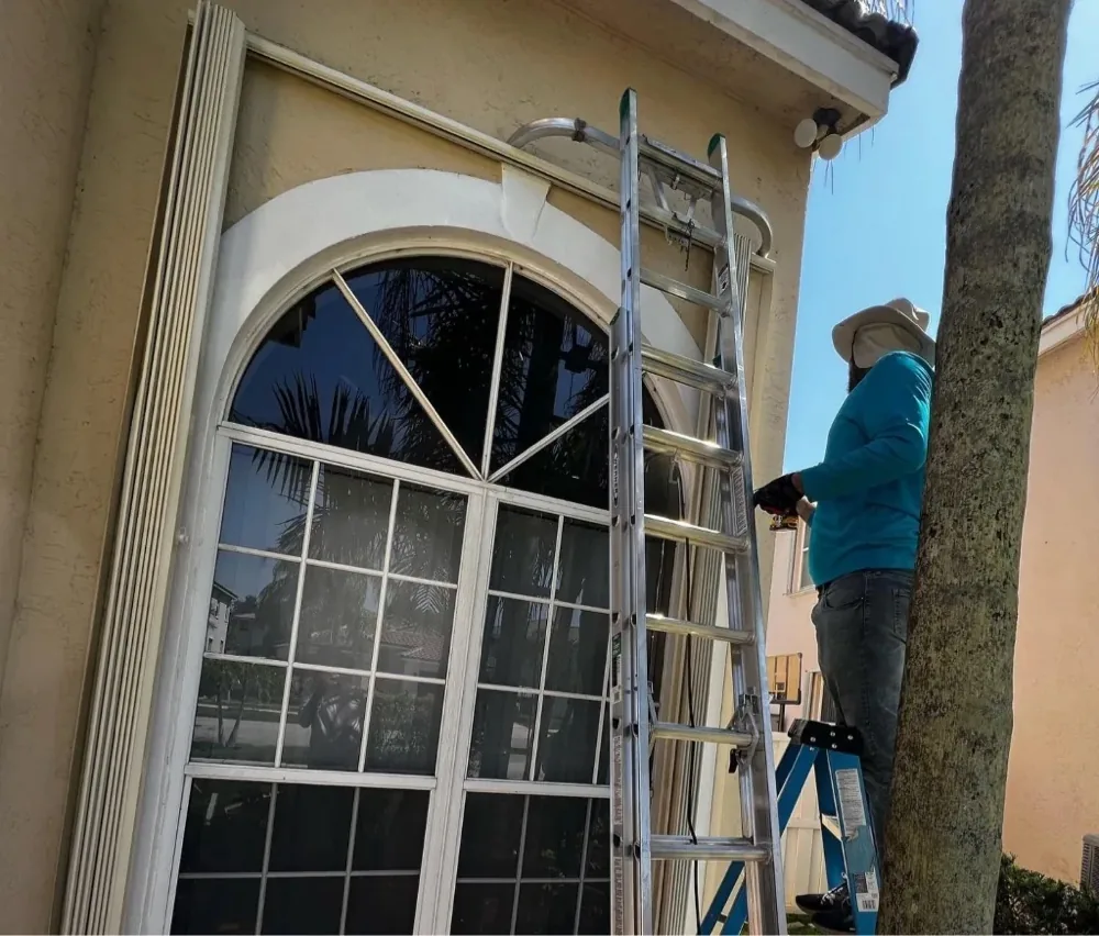 Installer working on accordion shutters above an arched window on a Miami-Dade home